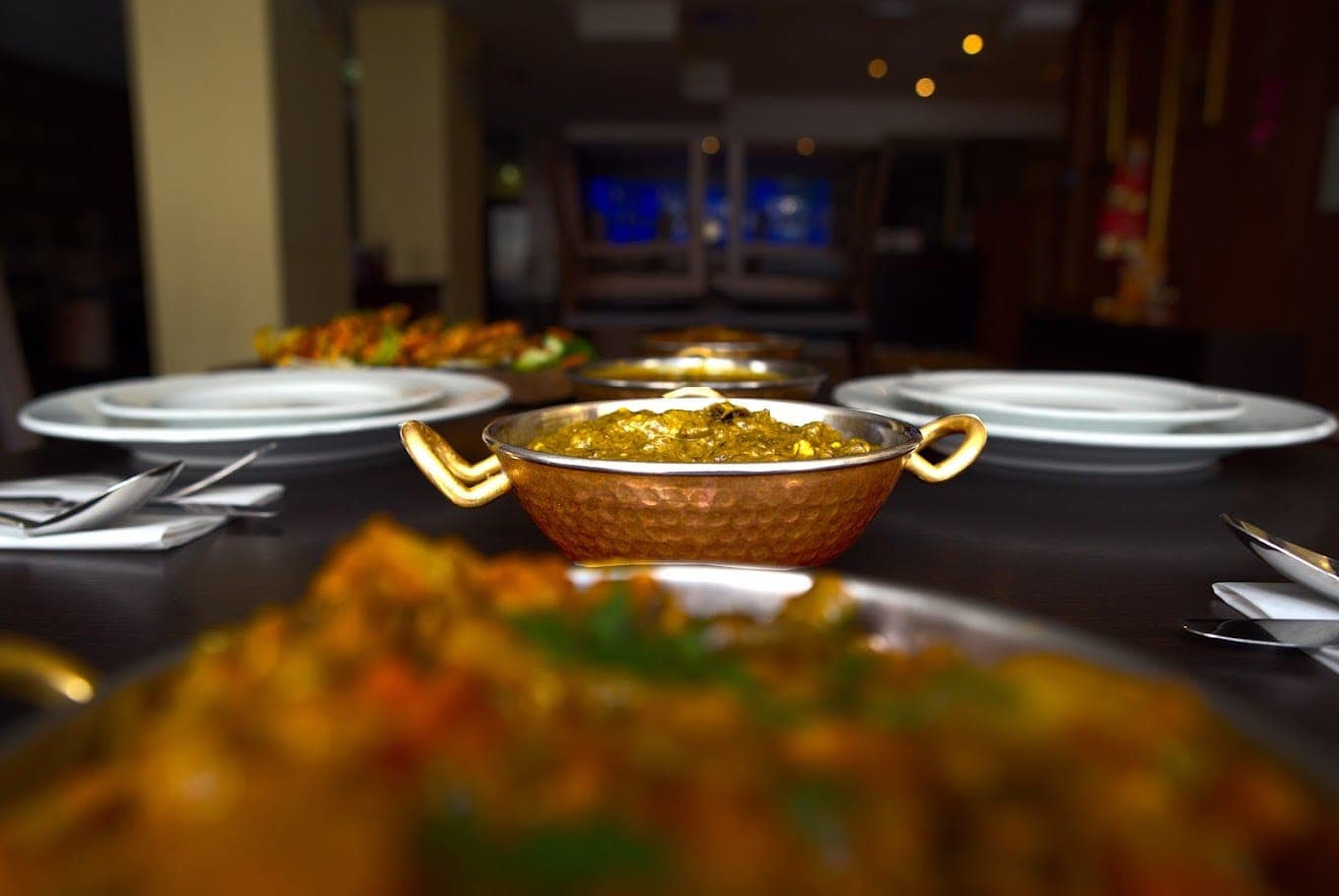 Gedeckter Tisch mit Curry im Kupfer-Karahi im Gastraum von Kirti's Dhaba